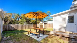 A backyard with a picnic table and an umbrella, surrounded by a wooden fence and a small shed. - Cheerful Coastal Home Close to Beach (Palm Harbor)