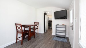 Cocina compacta con comedor, horno empotrado y televisor montado en la pared.