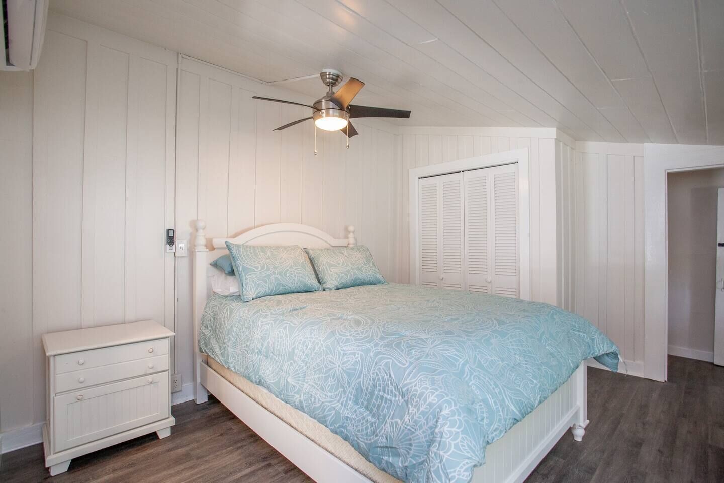 Une chambre à coucher comprenant un lit, une table de chevet, un ventilateur de plafond et un dressing.