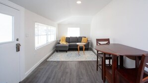Una habitación con un sofá gris, una mesita redonda pequeña y una mesa de comedor de madera.