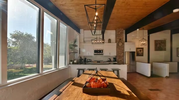 Une cuisine moderne avec de grandes fenêtres, une table à manger en bois et un luminaire suspendu.