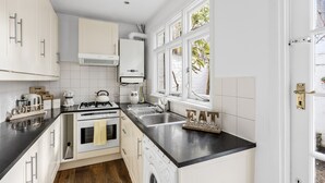 A compact kitchen with white cabinets, a black countertop, a built-in oven, a washing machine, and a window with a view of greenery.