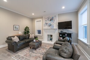 A living room with a sectional sofa, a fireplace, a television, and a large window. - Historic Haven | JZ Vacation Rentals (St. Louis)