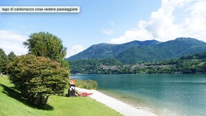 A lakeside view with a boat dock, grassy area, and mountains in the background. - Dolomia rosmini (Trento)