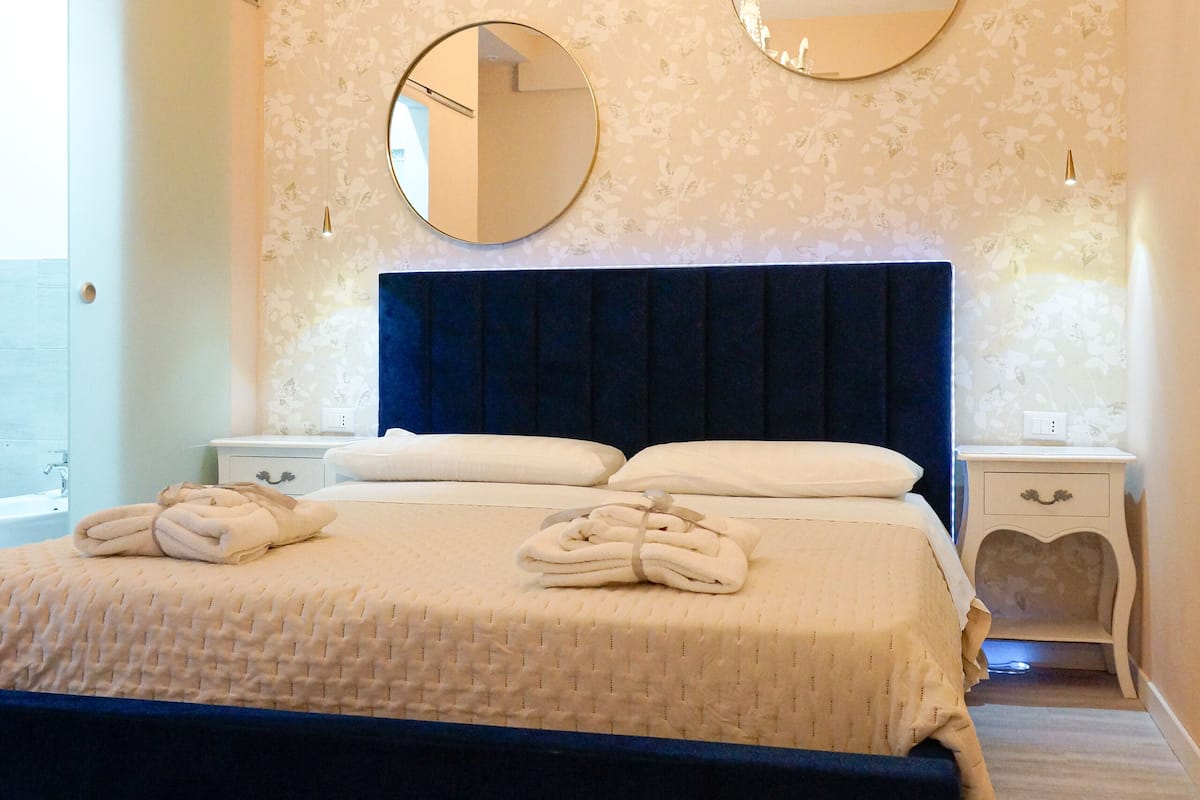 A bedroom with a large bed, two bedside tables, a chandelier, and a large mirror on the wall.