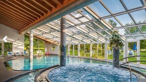 An indoor swimming pool with a glass ceiling, surrounded by lounge chairs and a view of the outdoors. - Dolomia rosmini (Trento)
