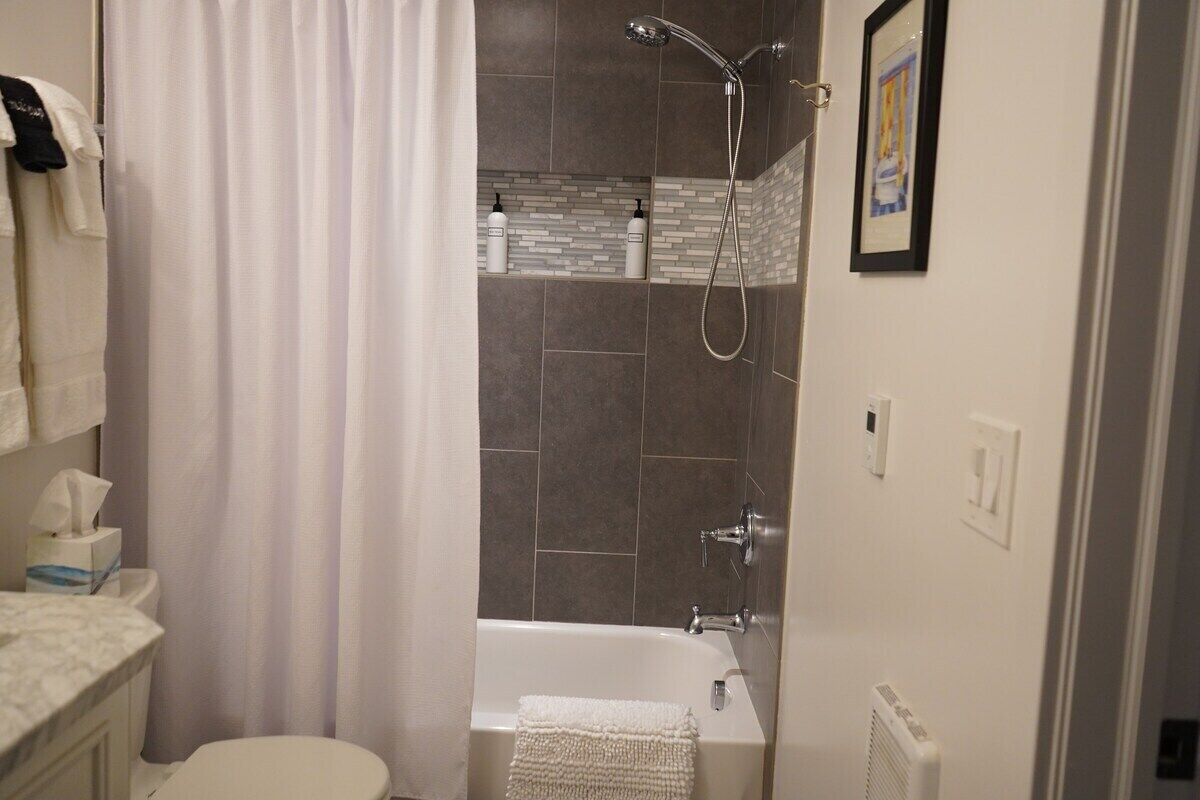 A bathroom with a bathtub, shower, and toilet. There are towels hanging on the wall and a framed picture on the wall.