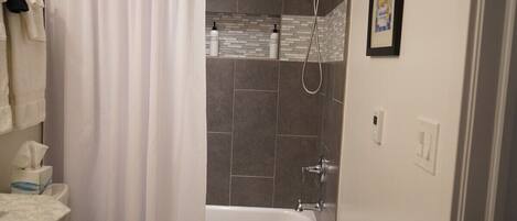 A bathroom with a bathtub, shower, and toilet. There are towels hanging on the wall and a framed picture on the wall.