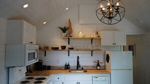 Une cuisine moderne avec des meubles blancs, un plan de travail en bois, une cuisinière encastrée, un four à micro-ondes, un lave-vaisselle et un luminaire suspendu.