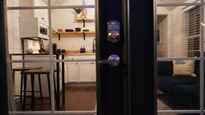 On aperçoit, à travers une porte, une pièce qui comprend une cuisine et un canapé de couleur sombre.