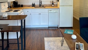 Une cuisine moderne avec des meubles blancs, un plan de travail en bois, un four encastré, un lave-vaisselle et un luminaire suspendu.