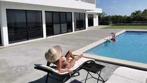 Une maison moderne avec une piscine, une personne qui prend un bain de soleil et un ciel dégagé.