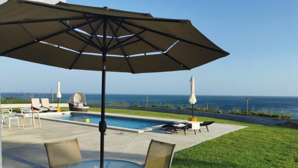 Un espace aménagé au bord de la piscine, avec une table et des chaises, un parasol et des chaises longues.