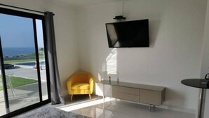Une chambre d’hôtel moderne avec un grand lit, un téléviseur fixé au mur, une chaise jaune et une console au design minimaliste.