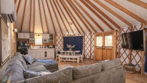 Un interior acogedor de una yurta con un sofá, una mesa de comedor y una zona de cocina.