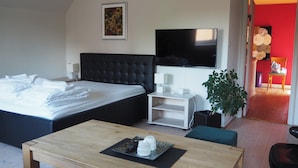 Ein modernes Hotelzimmer mit einem großen Bett, einem Flachbildfernseher, einem Nachttisch, einer kleinen Pflanze und einem Holztisch.