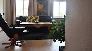 Ein Wohnzimmer mit einer schwarzen Ledersofa, einem Holztisch und einem Poster von Vincent van Goghs 'Café de Nuit'.