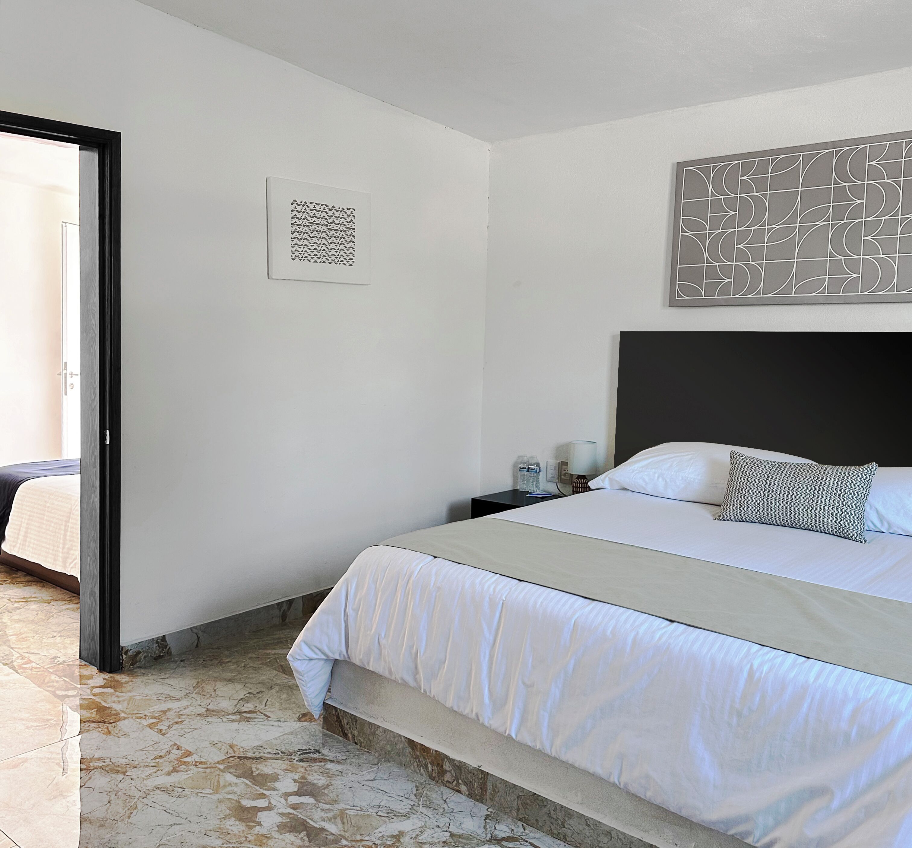 Habitación de hotel con una cama, una mesita de noche, una obra de arte en la pared y una puerta que da a un balcón.