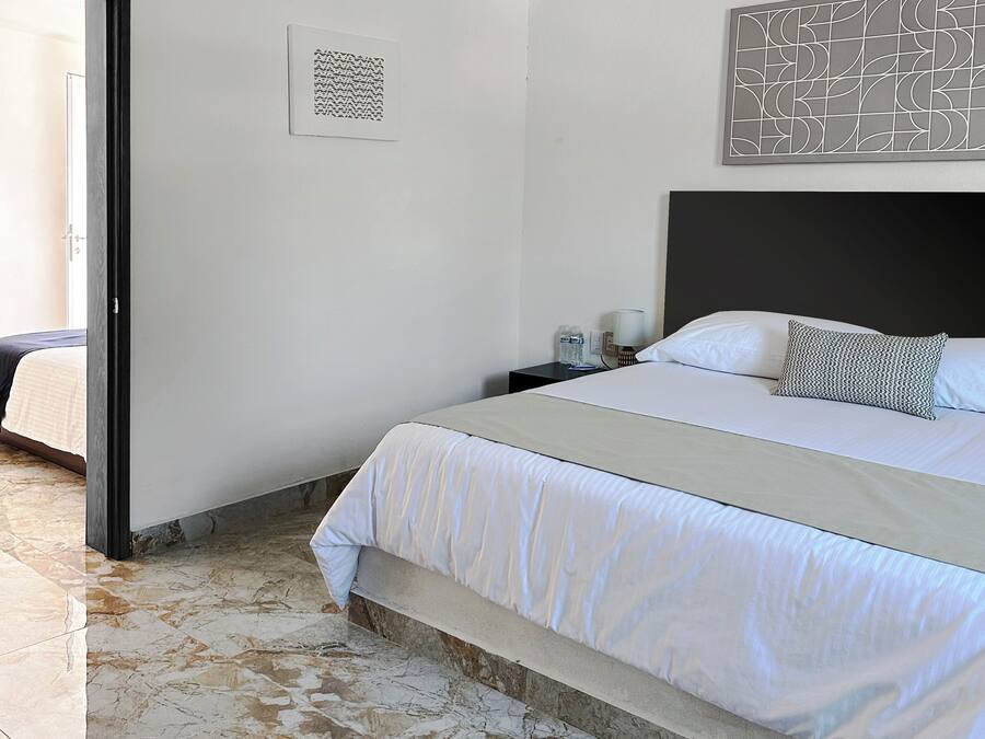 Habitación de hotel con una cama, una mesita de noche, una obra de arte en la pared y una puerta que da a un balcón.