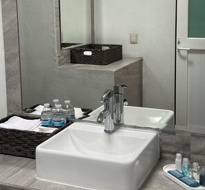 A modern bathroom with a large white sink, a mirror, and a wicker basket containing toiletries. - DUNAMIS HOTEL (Jilotepec)