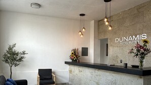 Un hall d’accueil moderne avec un sol en marbre, un canapé noir agrémenté de coussins bleus, une chaise en bois et un comptoir d’accueil orné d’un vase de fleurs.