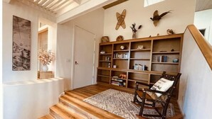 Eine Treppe führt zu einem Wohnbereich mit Holzboden, einem Schaukelstuhl, einem Bücherregal und Wanddekoration.