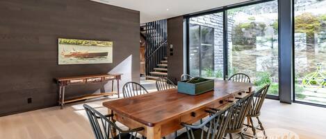 Un'area pranzo moderna con tavolo e sedie in legno, una scala e ampie finestre che offrono vista all'esterno.
