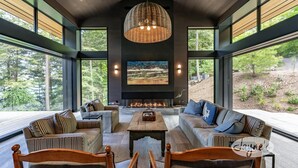 Una sala de estar moderna con una chimenea grande, asientos cómodos y ventanas amplias que ofrecen vistas al exterior.