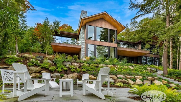 Una casa moderna con fachada de piedra, ventanas amplias y una terraza de madera con sillas Adirondack.