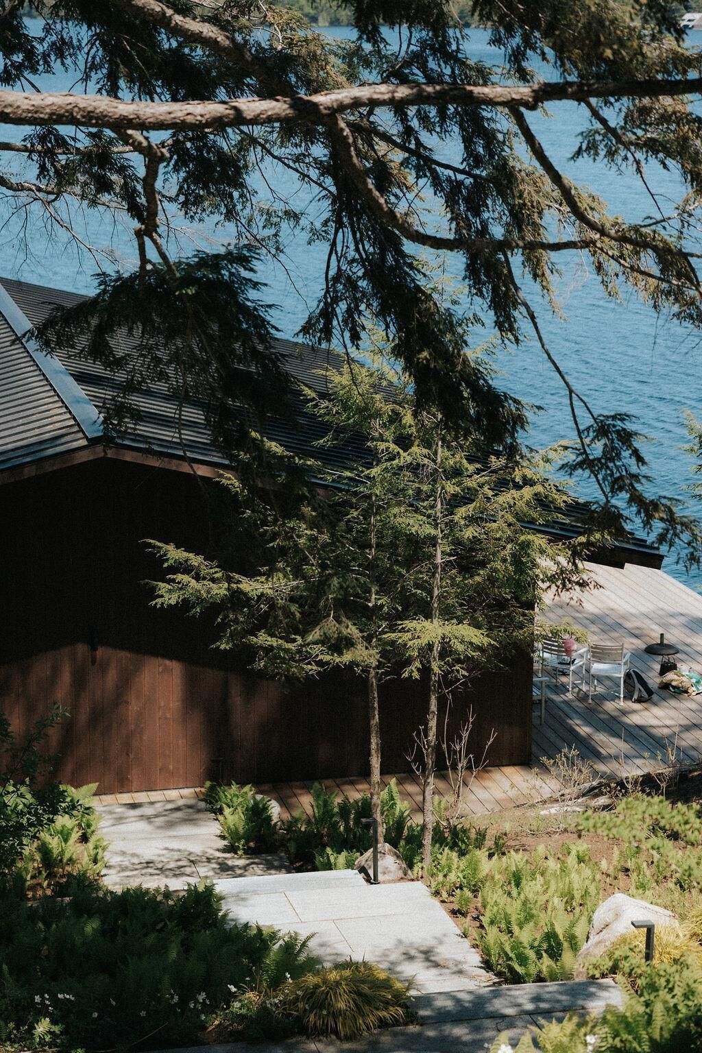 Una cabaña de madera con techo metálico, un muelle con sillas y una vista despejada del agua.