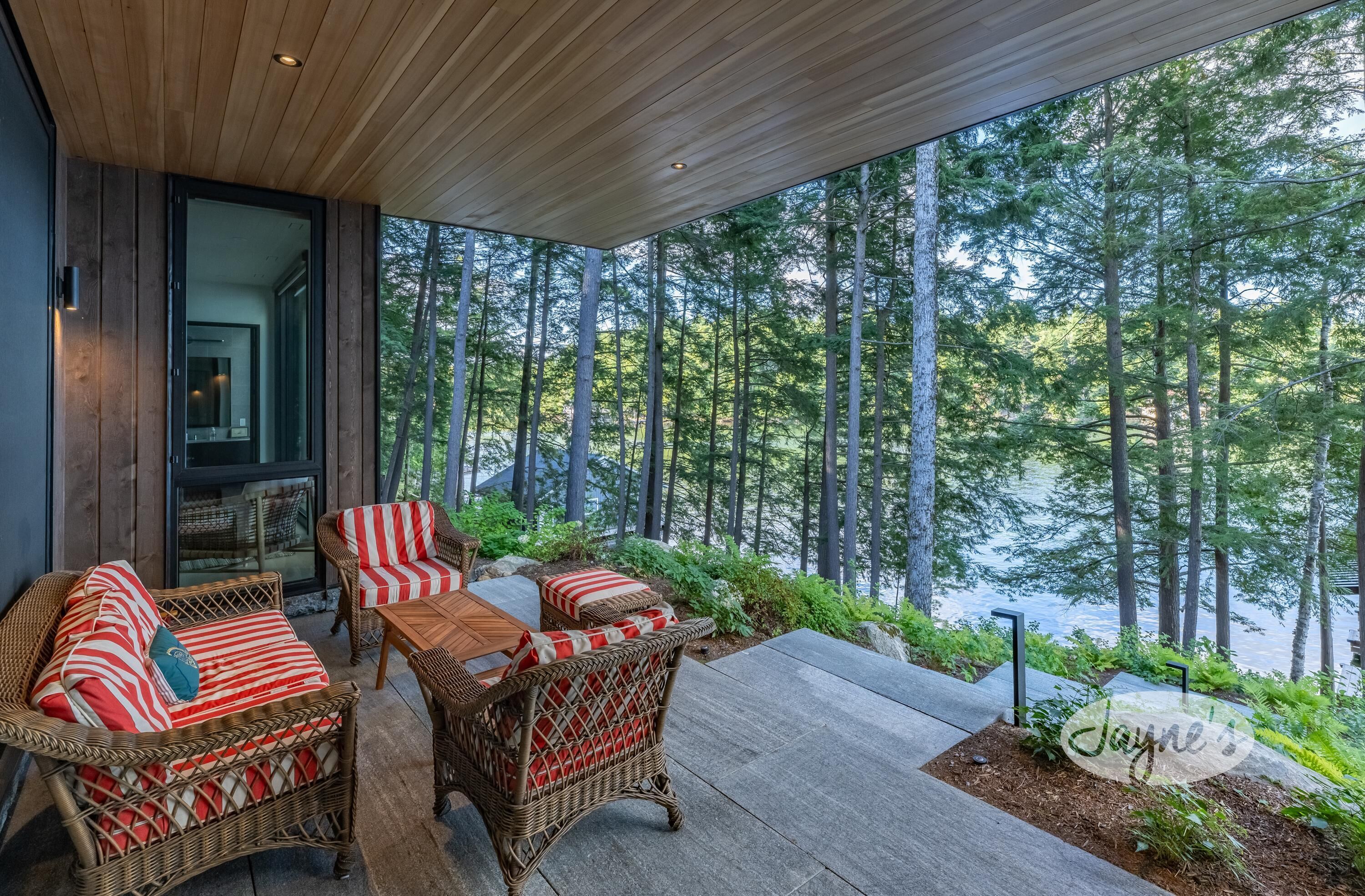 A covered outdoor seating area with wicker furniture and a view of a forest.