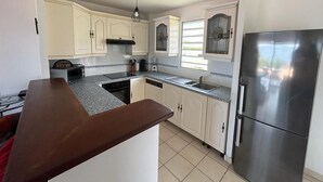 A modern kitchen with white cabinets, a stainless steel refrigerator, and a granite countertop. - T3 vue mer sur les Caraïbes (Les Trois-Îlets)