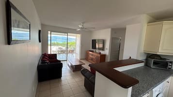 A spacious living area with a sliding glass door leading to a balcony, a kitchen with a built-in oven and microwave, and a small seating area with a sofa and a coffee table.