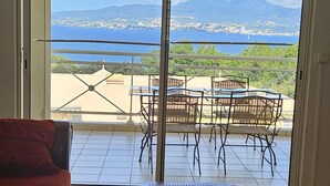 A living room with a red sofa, a wooden coffee table, and a view of a balcony with outdoor furniture. - T3 vue mer sur les Caraïbes (Les Trois-Îlets)