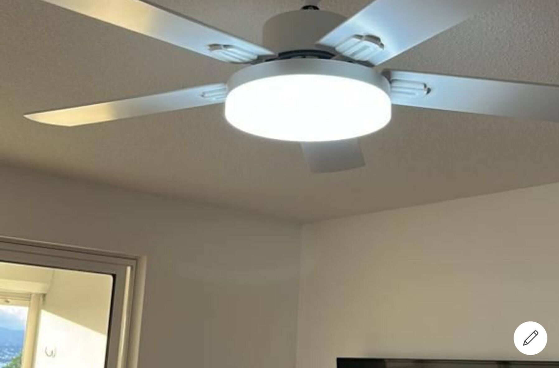 A ceiling fan with a light fixture in a room with plain walls and a door leading to a balcony.