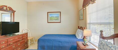 Ett sovrum med två sängar, en tv på en byrå och ett fönster med persienner.