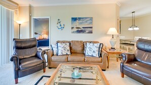 A living room with a brown leather sofa, a glass coffee table, and a painting of a lighthouse. - Myrtle Beach Condo w/ Community Perks (Myrtle Beach)
