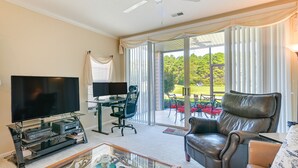 A living room with a flat-screen TV, a glass coffee table, a leather sofa, and a sliding glass door leading to a patio with outdoor furniture. - Myrtle Beach Condo w/ Community Perks (Myrtle Beach)