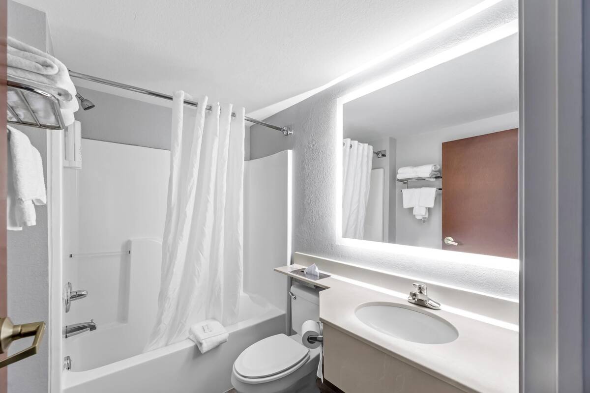 Une salle de bain moderne équipée d’une baignoire, de toilettes et d’un lavabo, avec un grand miroir et un porte-serviettes.