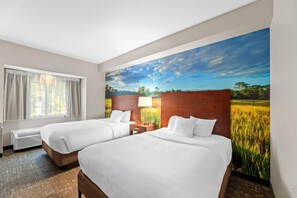 A hotel room with two beds, a window with curtains, a wall-mounted lamp, and a large painting of a field.
