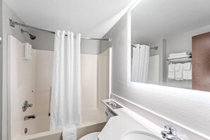 A modern bathroom with a bathtub, shower, toilet, and a large mirror. - Clarion Pointe Starkville near University (Starkville)