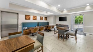 Uma área de refeições moderna com mesas e cadeiras de madeira, um banco acolchoado azul e uma TV de tela plana na parede.