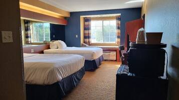 A hotel room with two beds, a desk, a coffee machine, and a window with curtains.