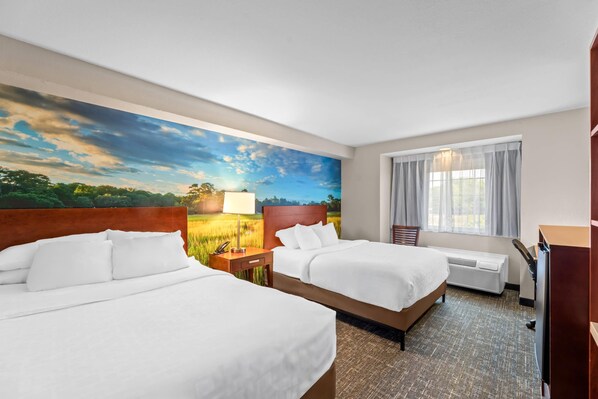 A hotel room with two beds, a large window with curtains, a painting of a landscape, and a desk with a lamp.