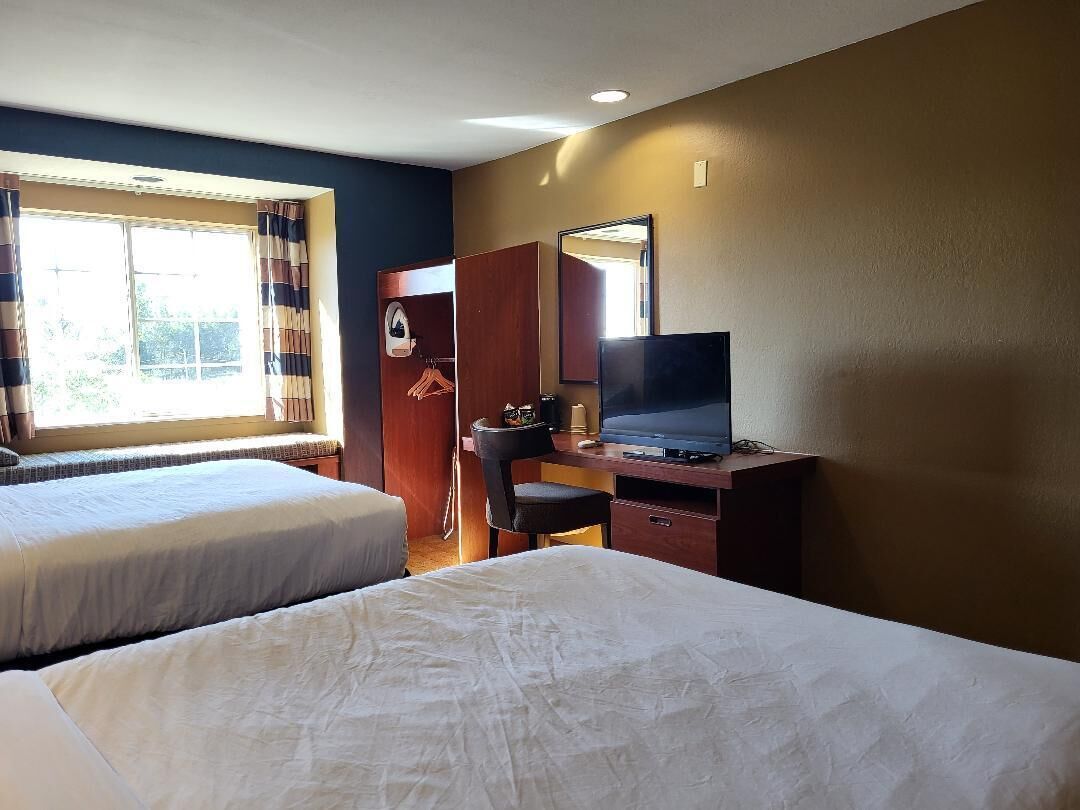 Ein Hotelzimmer mit zwei Betten, einem Schreibtisch mit Fernseher und einem Kleiderschrank.