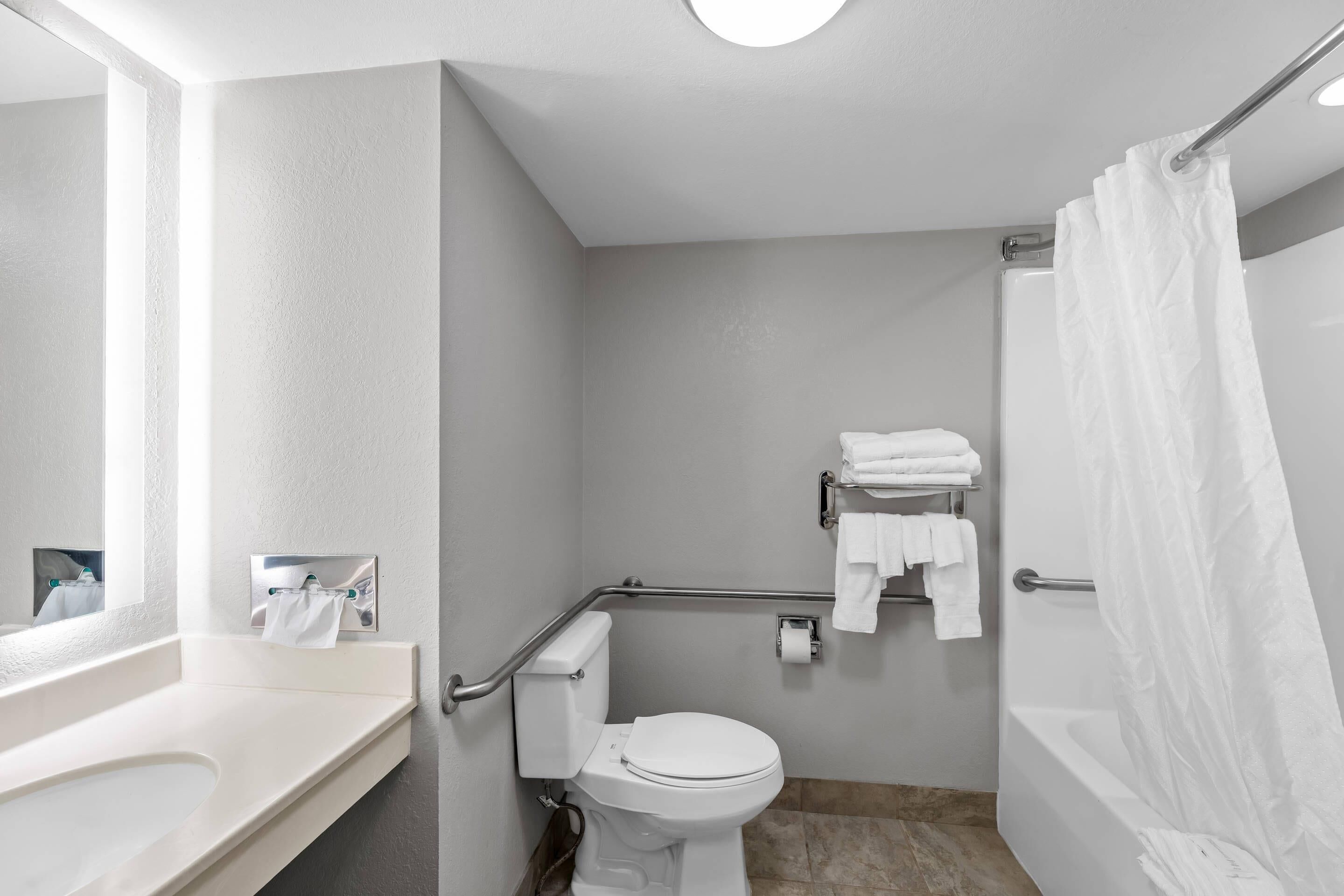 Un baño con lavamanos, inodoro y bañera blancos, equipado con barras de apoyo y cortina de ducha.