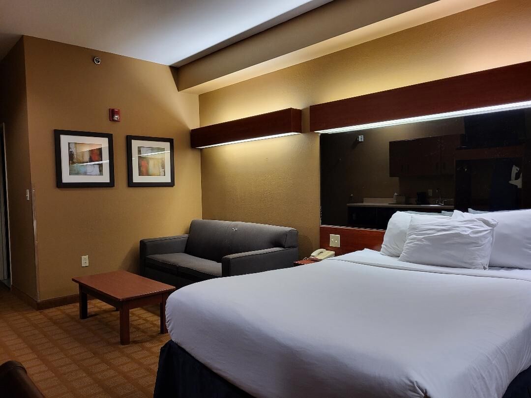 Quarto de hotel com uma cama, um sofá, uma mesinha e duas fotografias emolduradas na parede.