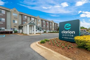 A hotel entrance with a sign for Clarion Pointe by Choice Hotels, featuring a modern building facade, a parking area, and landscaped greenery.