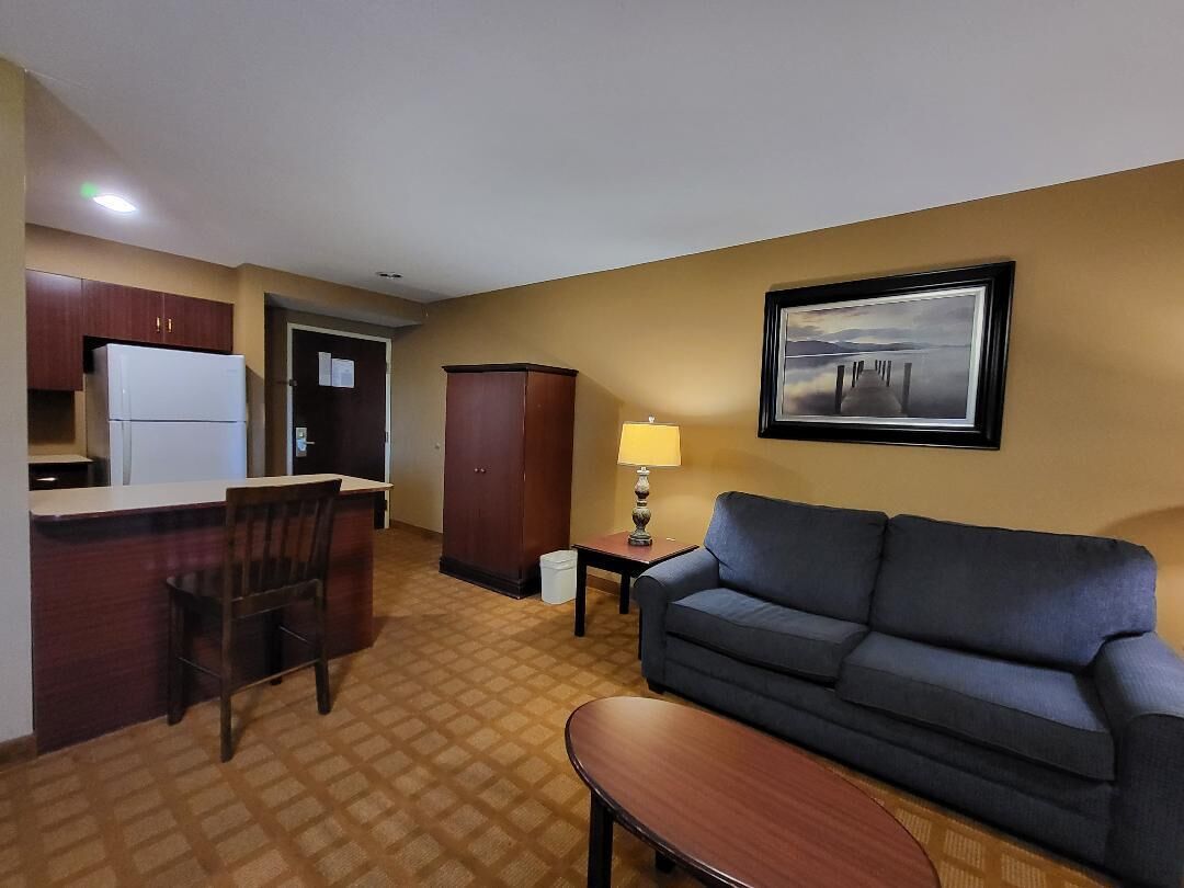 Een hotelkamer met een kitchenette, een bank, een eettafeltje en een lijst met een afbeelding aan de muur.