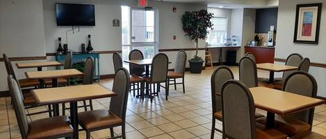 A restaurant with multiple tables and chairs, a television mounted on the wall, and a potted plant.